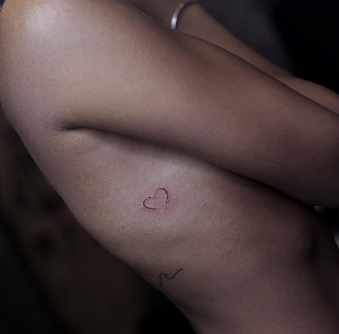 Delicate red fine line heart tattoo on the thigh